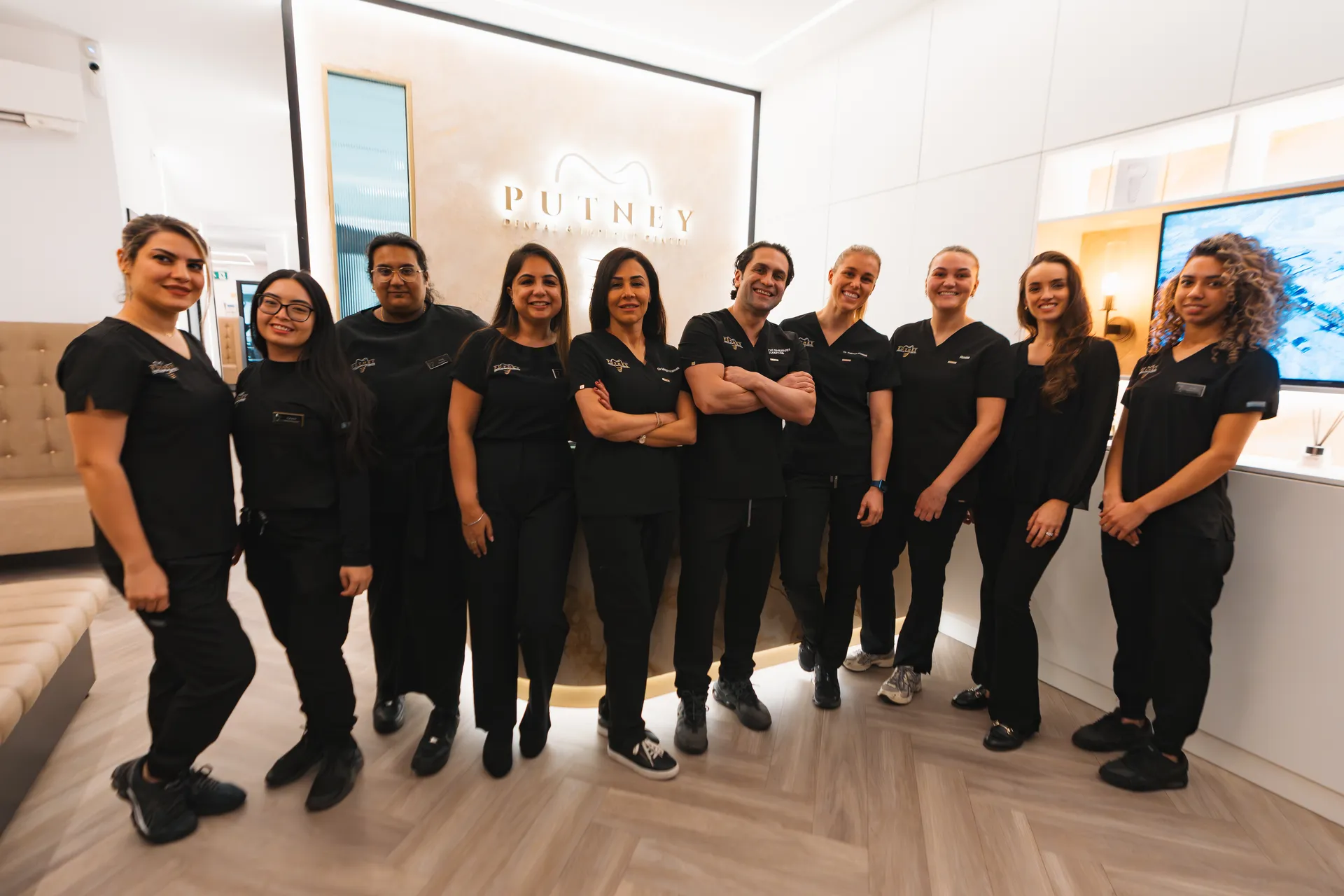 Group of ten dental professionals standing inside Putney Dental & Implant Centre wearing black uniforms and smiling.