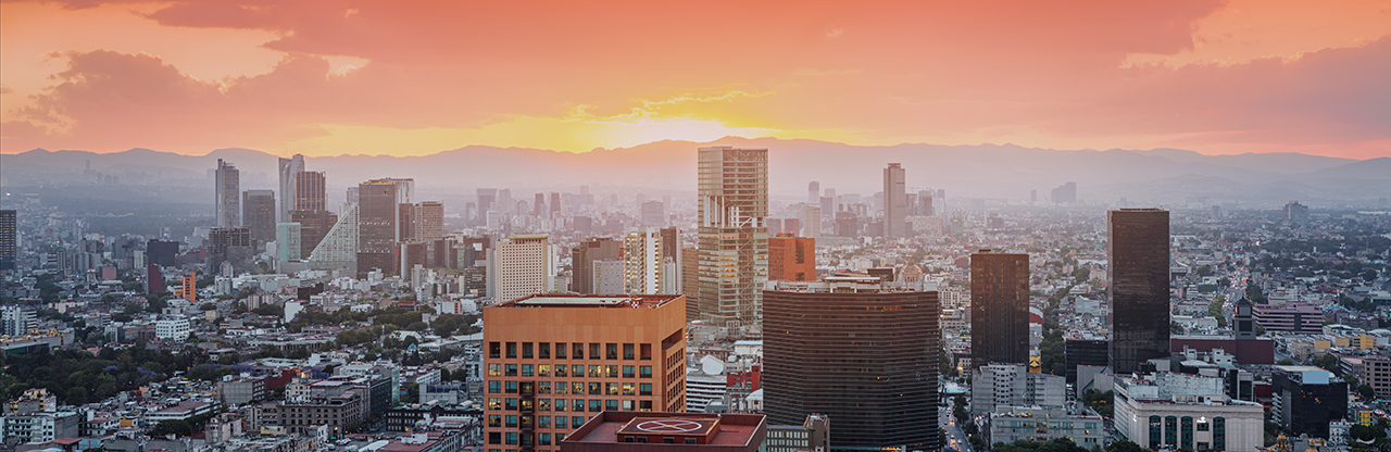 Cityscape of a modern urban area at sunset with numerous skyscrapers and mountains in the background.