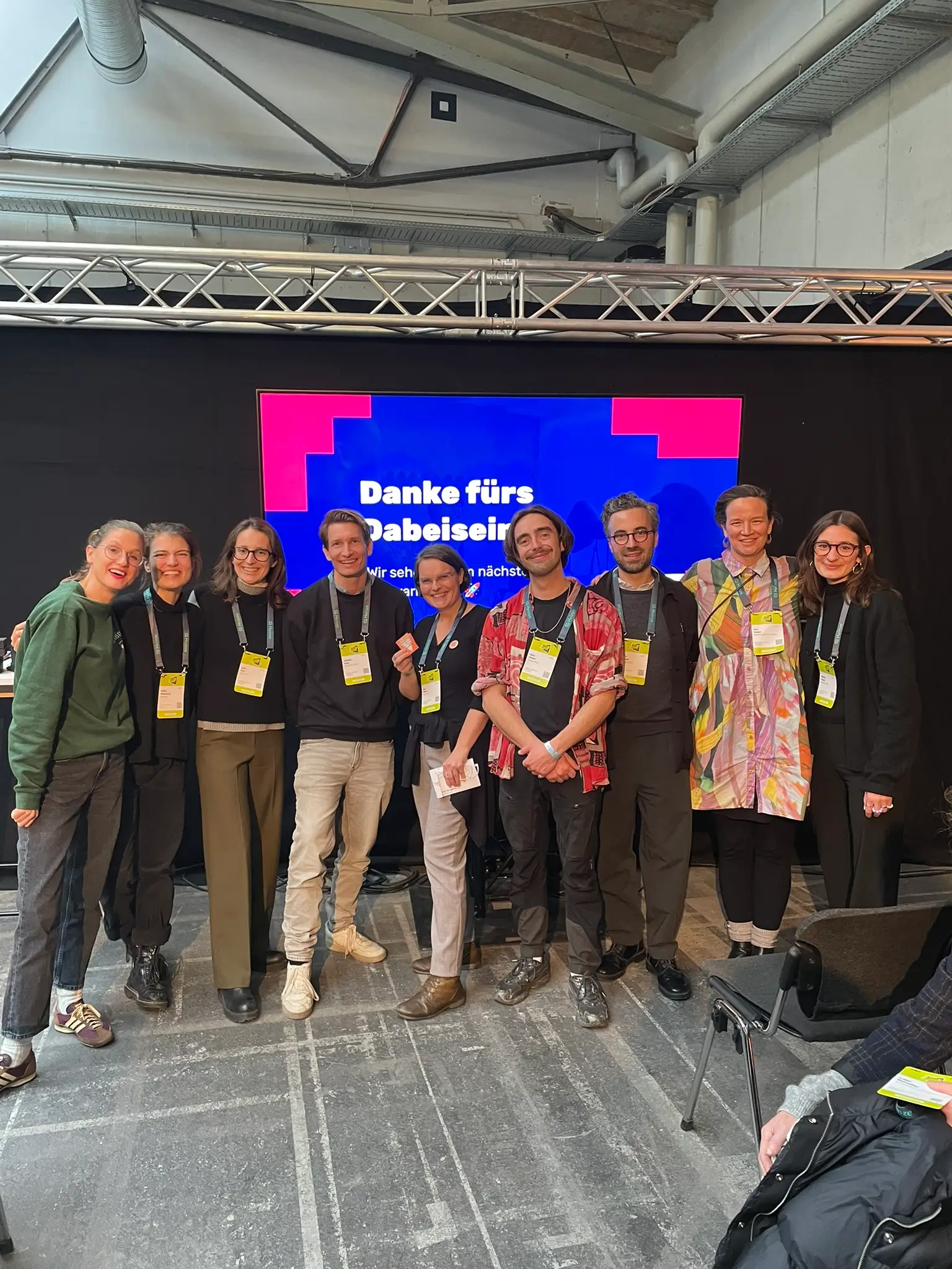 Gruppenfoto eines engagierten Teams beim Klimafestival in Berlin: Mehrere Teilnehmerinnen und Teilnehmer posieren gemeinsam vor einer Bühne mit Dankesbotschaft und tragen Festival-Badges.