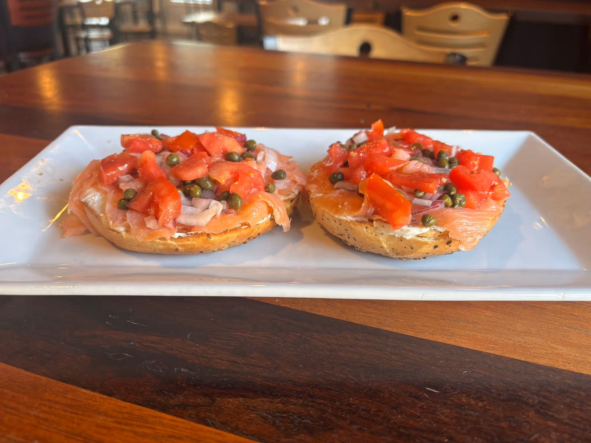 Two open faced sandwiches with tomatoes and peppers on a white plate.