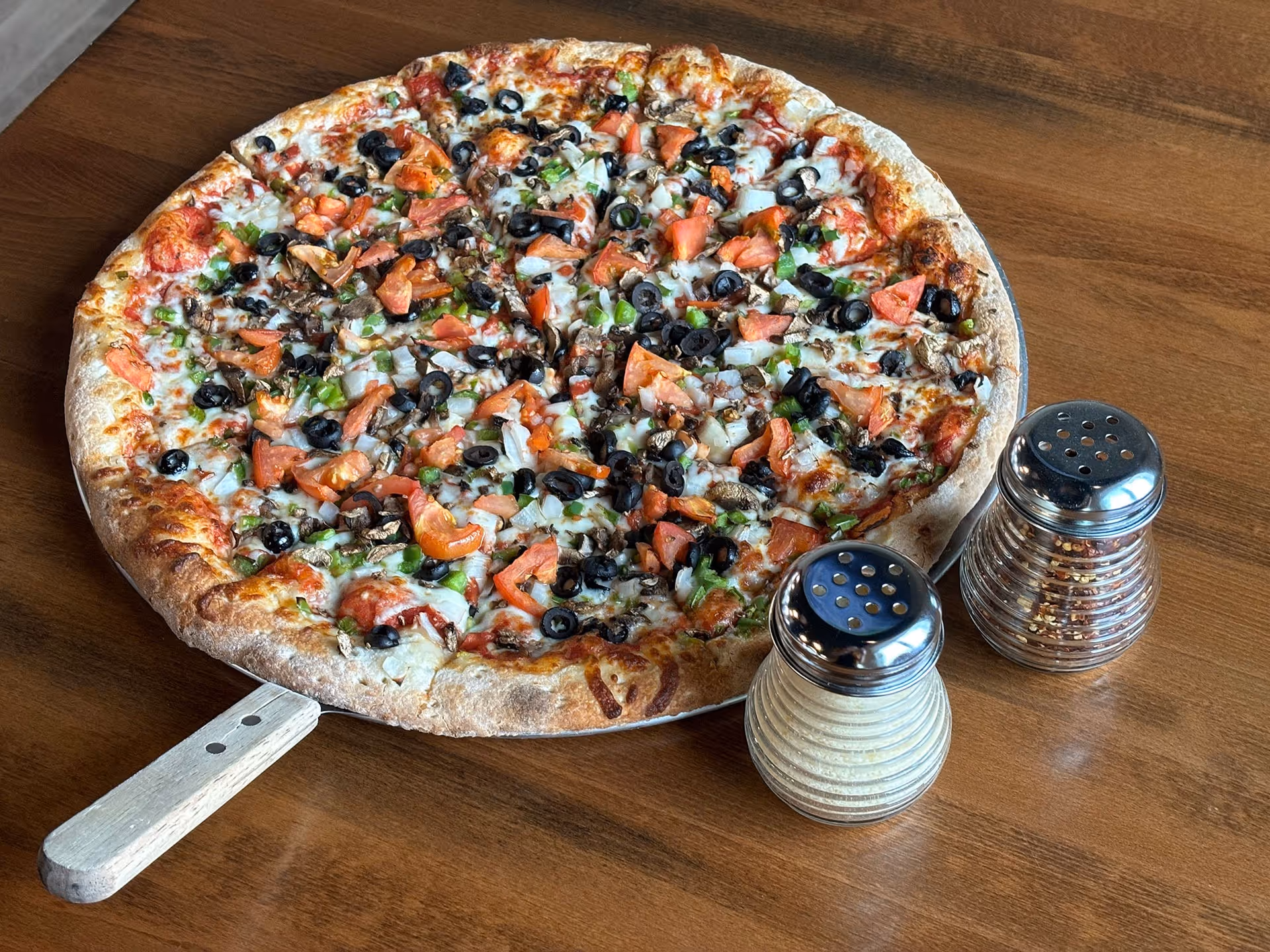 A pizza with black olives and tomatoes on a wooden table.