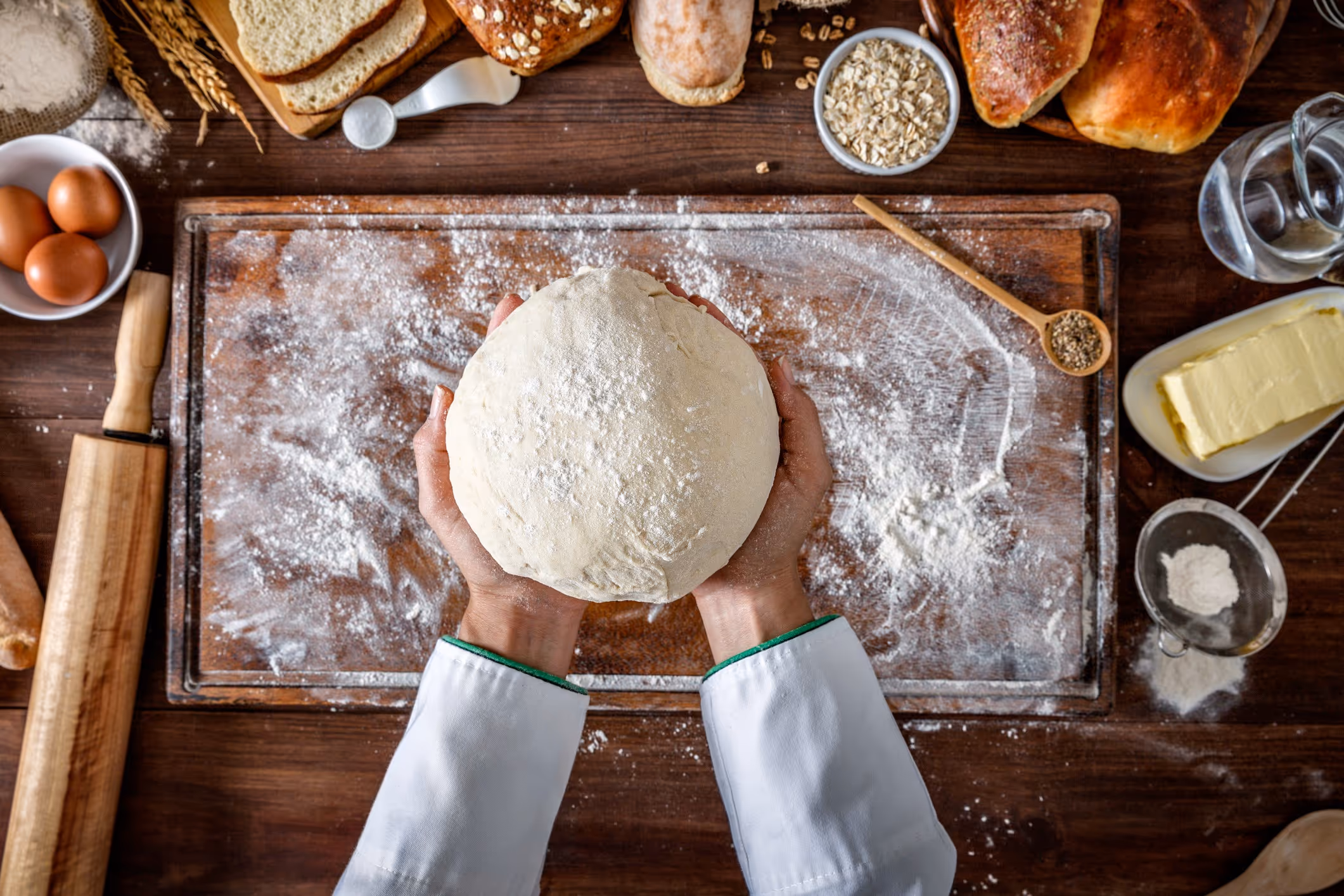 A person holding a dough ball on a wooden table.