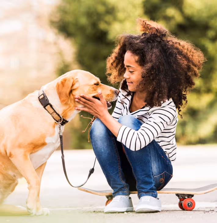 Girl squatting by a lab dog and holding its face while looking at the dog