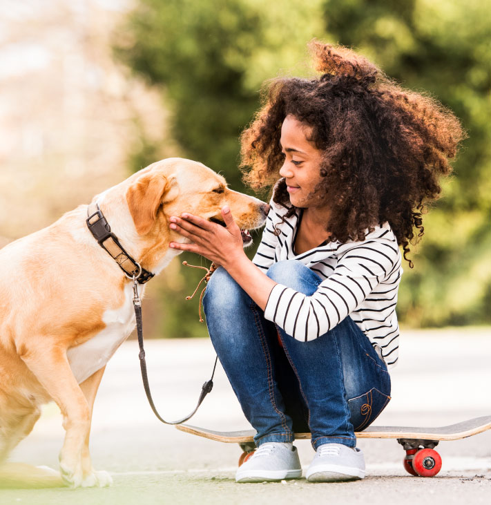Girl squatting by a lab dog and holding its face while looking at the dog