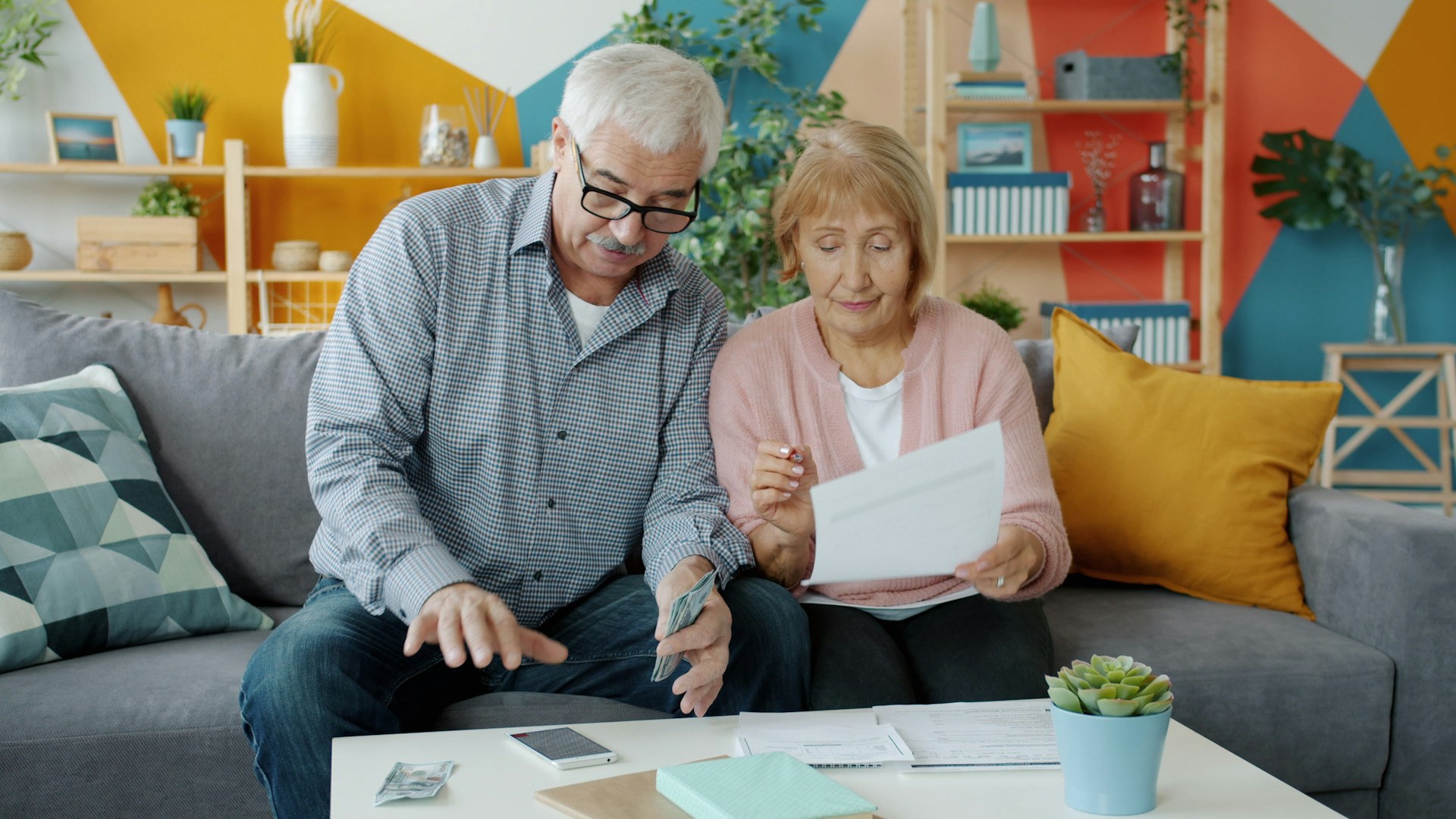 Elderly couple sitting on the couch holding money and documents