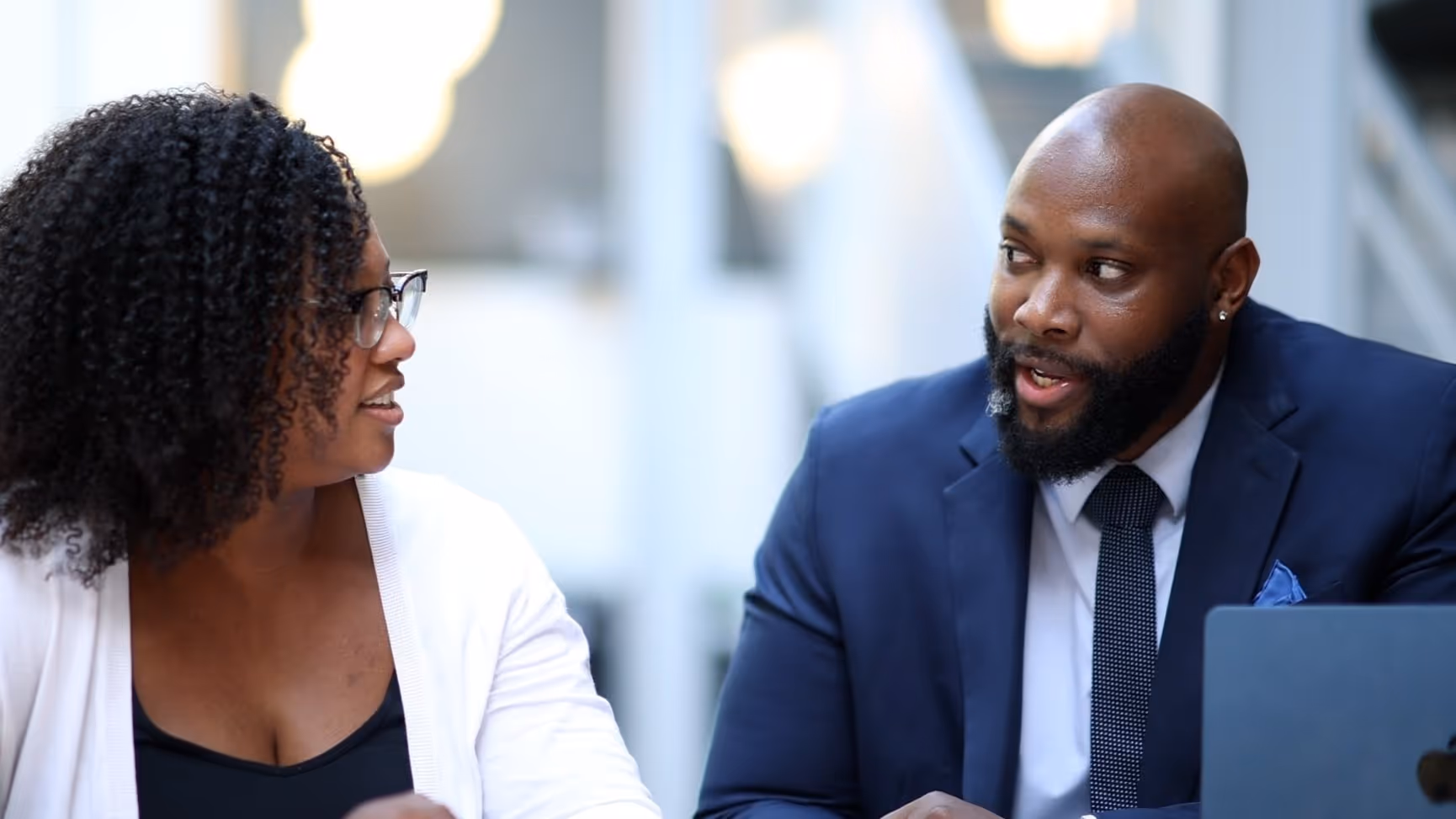 Two professionals in business attire having a conversation outdoors in an urban setting.