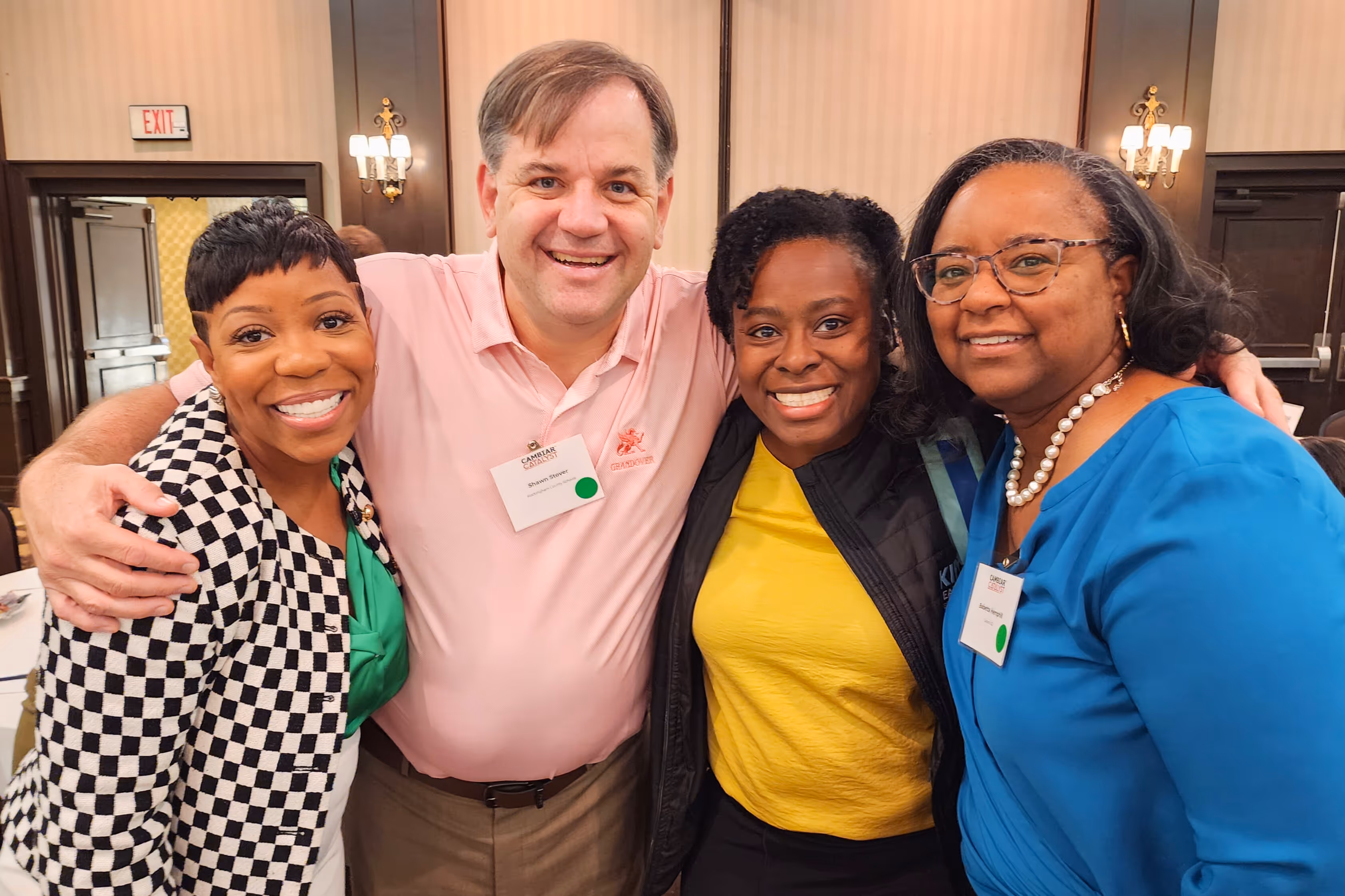 Four smiling people posing together at an indoor event in an elegant venue