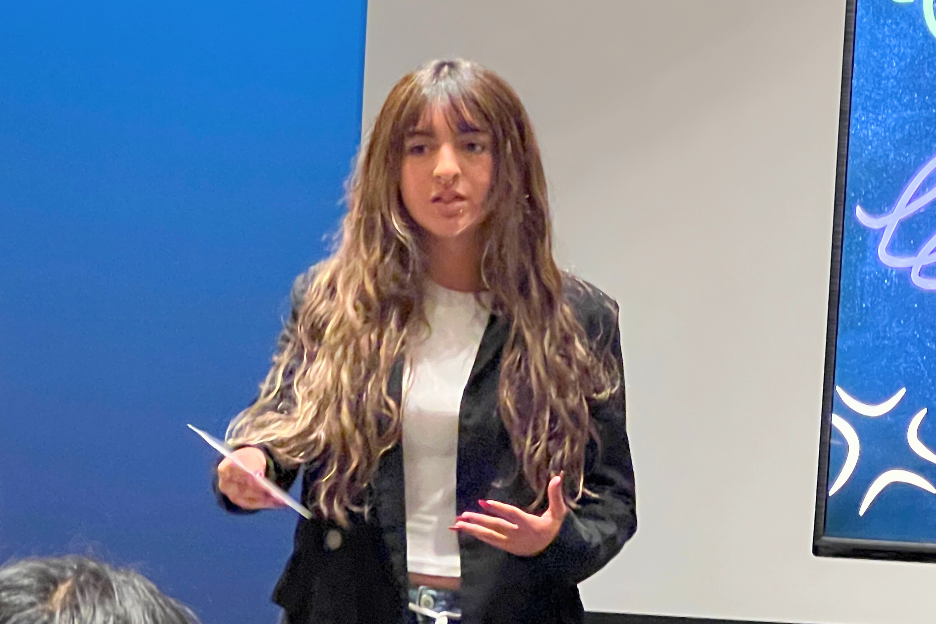 Student giving presentation on stage with blue background and screens