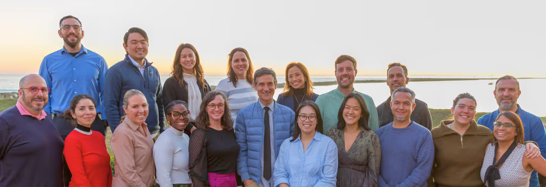 Regional fellowship colleagues standing together outdoors at sunset by water.