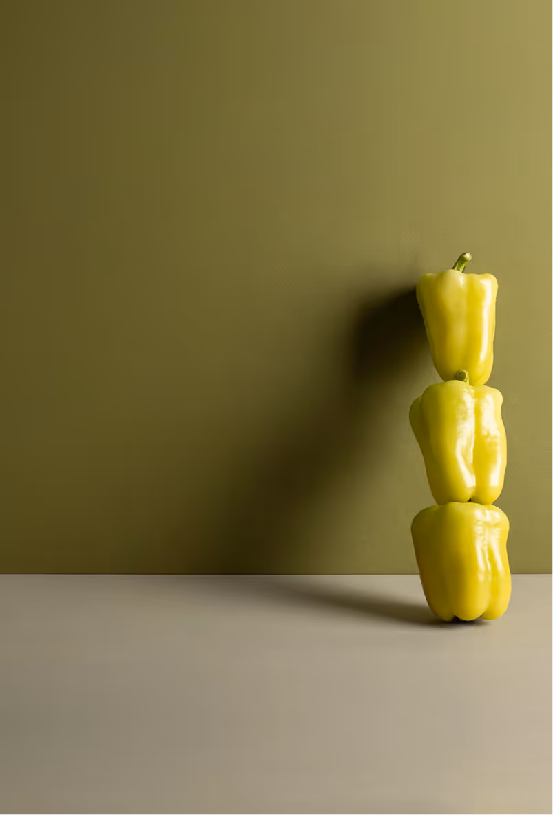 Stack of three yellow bell peppers against an olive green background with a gray surface.