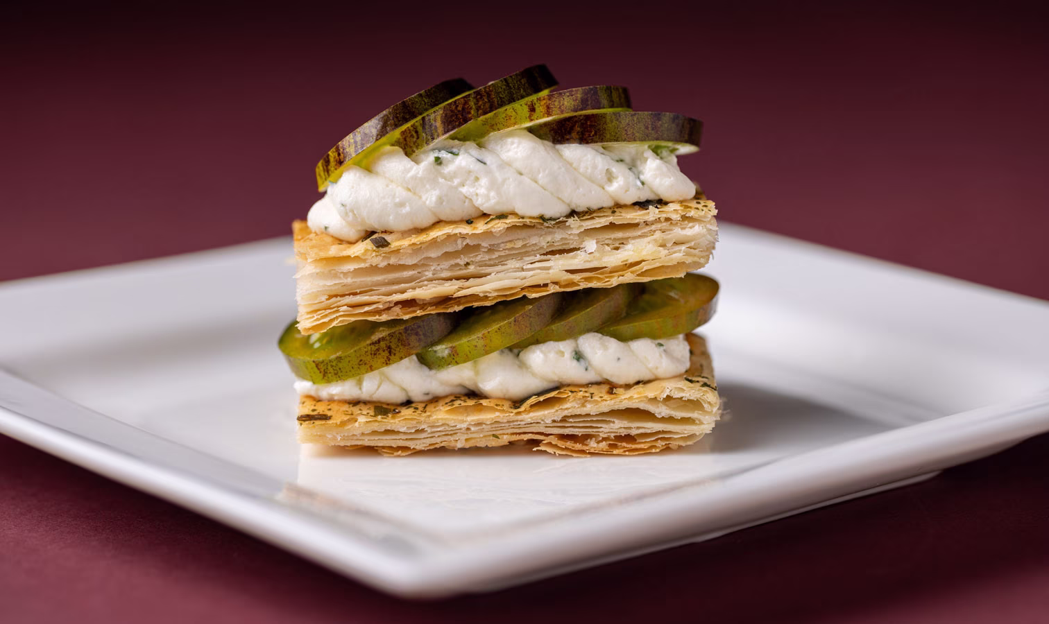 Layered millefoglie with whipped cream and Midnight plum slices on a white plate.