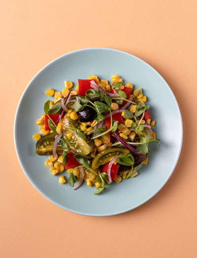 Kid's hand holding a small Popits cucumber between thumb and index finger against a beige background.