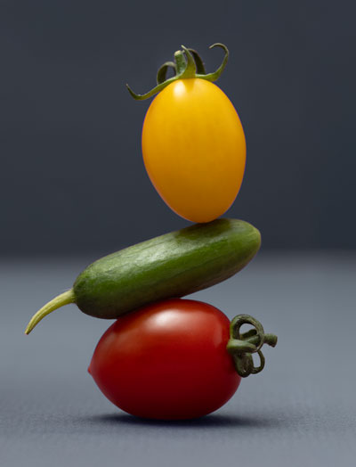 White plate with a salad of halved red and yellow cherry tomatoes, cucumber pieces, white cheese chunks, and fresh mint leaves on a dark purple background.