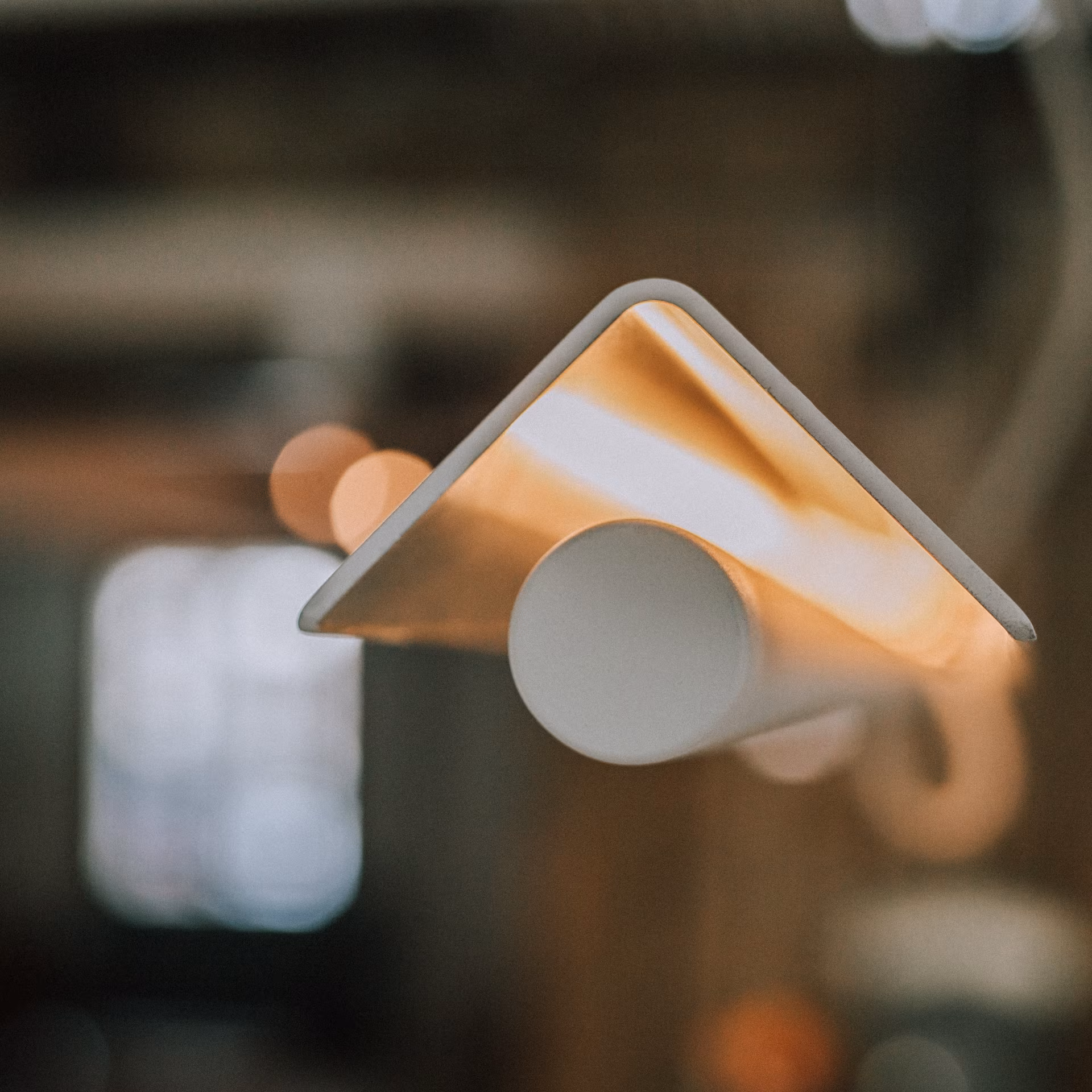 Lampe suspendue avec un abat-jour triangulaire blanc illuminé à l'intérieur.