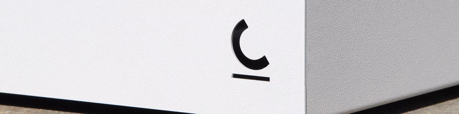 Coin d'un mur blanc avec un symbole noir minimaliste ressemblant à un C inversé au-dessus d'une ligne horizontale.