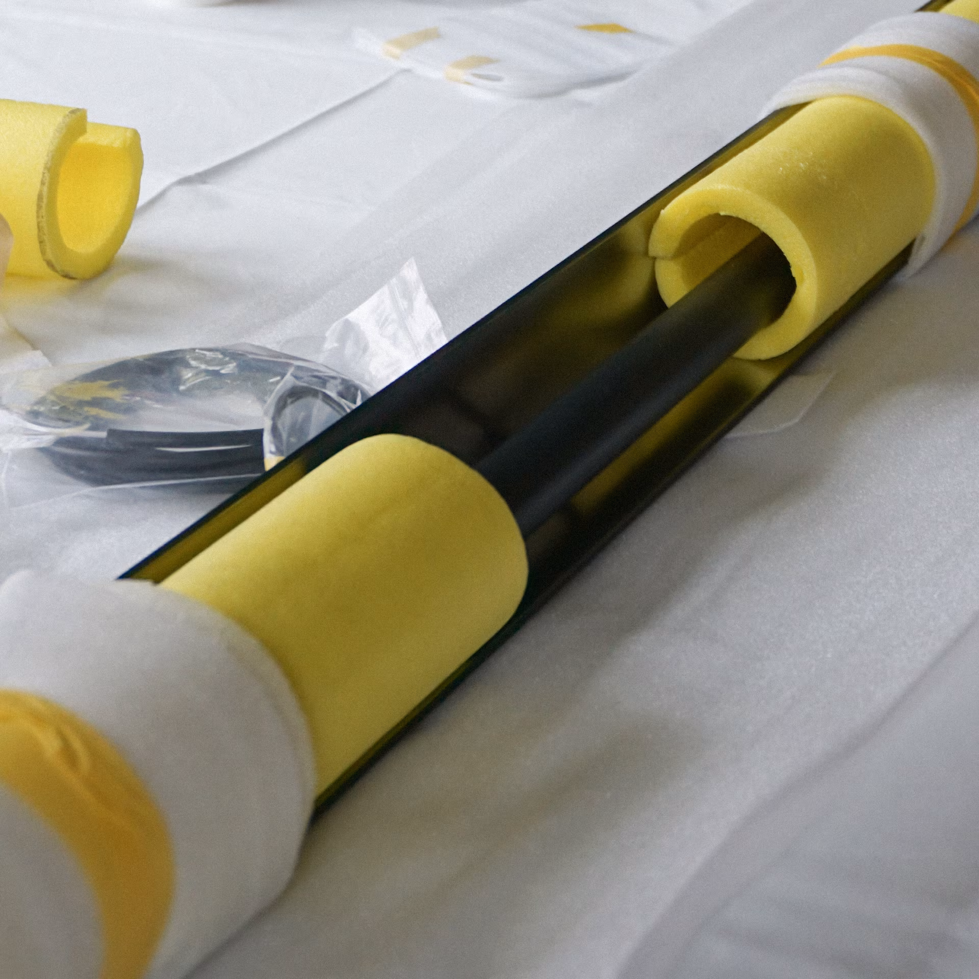 Tubulaire noir avec protections en mousse jaune posées sur un tissu blanc.