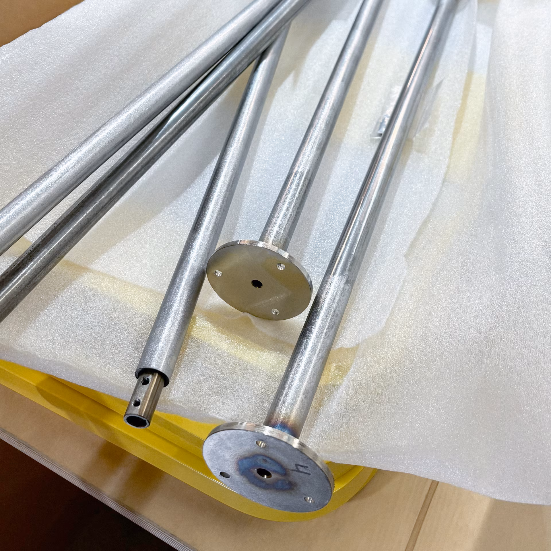 Plusieurs tubes métalliques cylindriques avec des plaques rondes à une extrémité, posés sur un film protecteur blanc sur une table.