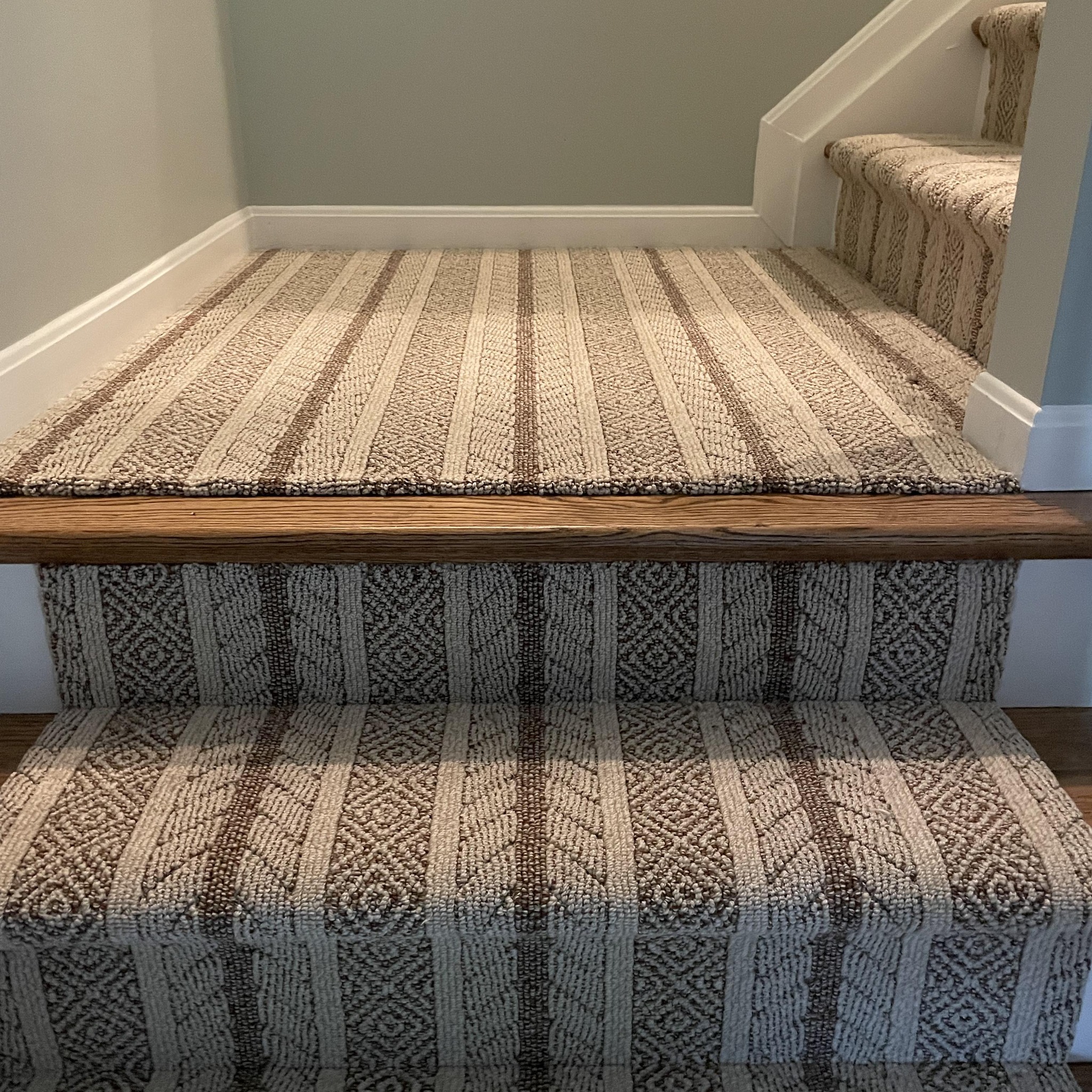 Carpeted stairs with a beige and brown striped pattern extending to a small landing area against light gray walls.