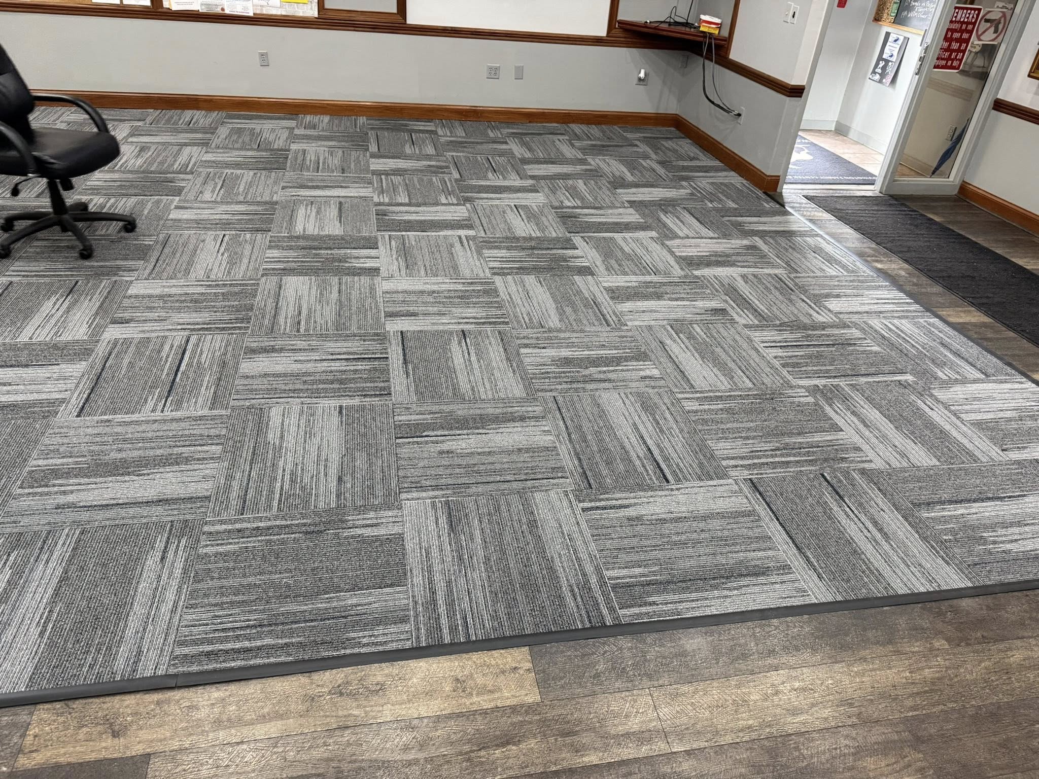 Office floor with gray commercial carpet tiles arranged in a checkerboard pattern next to wood-patterned laminate flooring.