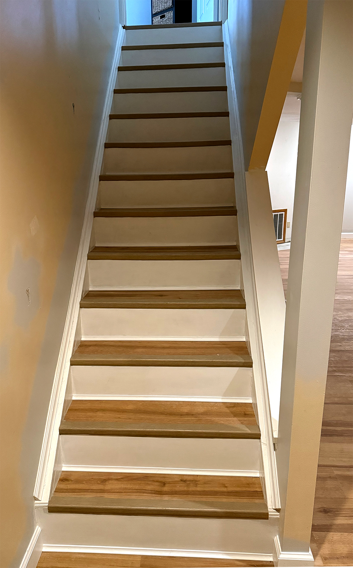 Indoor wooden stairs with white risers leading to a hallway with a door and baskets.