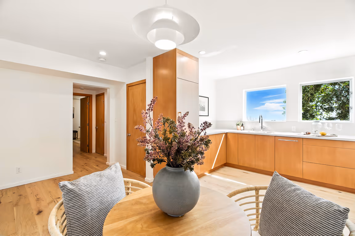 Modern kitchen with wooden cabinets, a round wooden table with a vase of flowers, and two chairs with striped cushions.