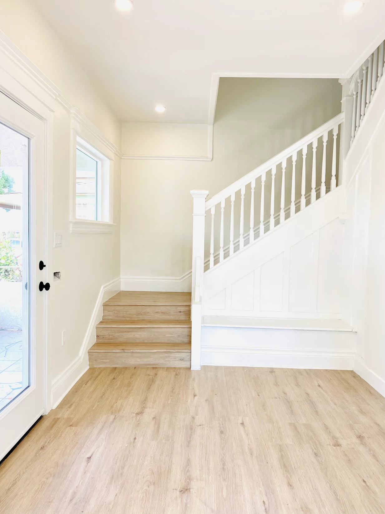 Bright room with light wood flooring, white stair railing, and a door with window leading outside.