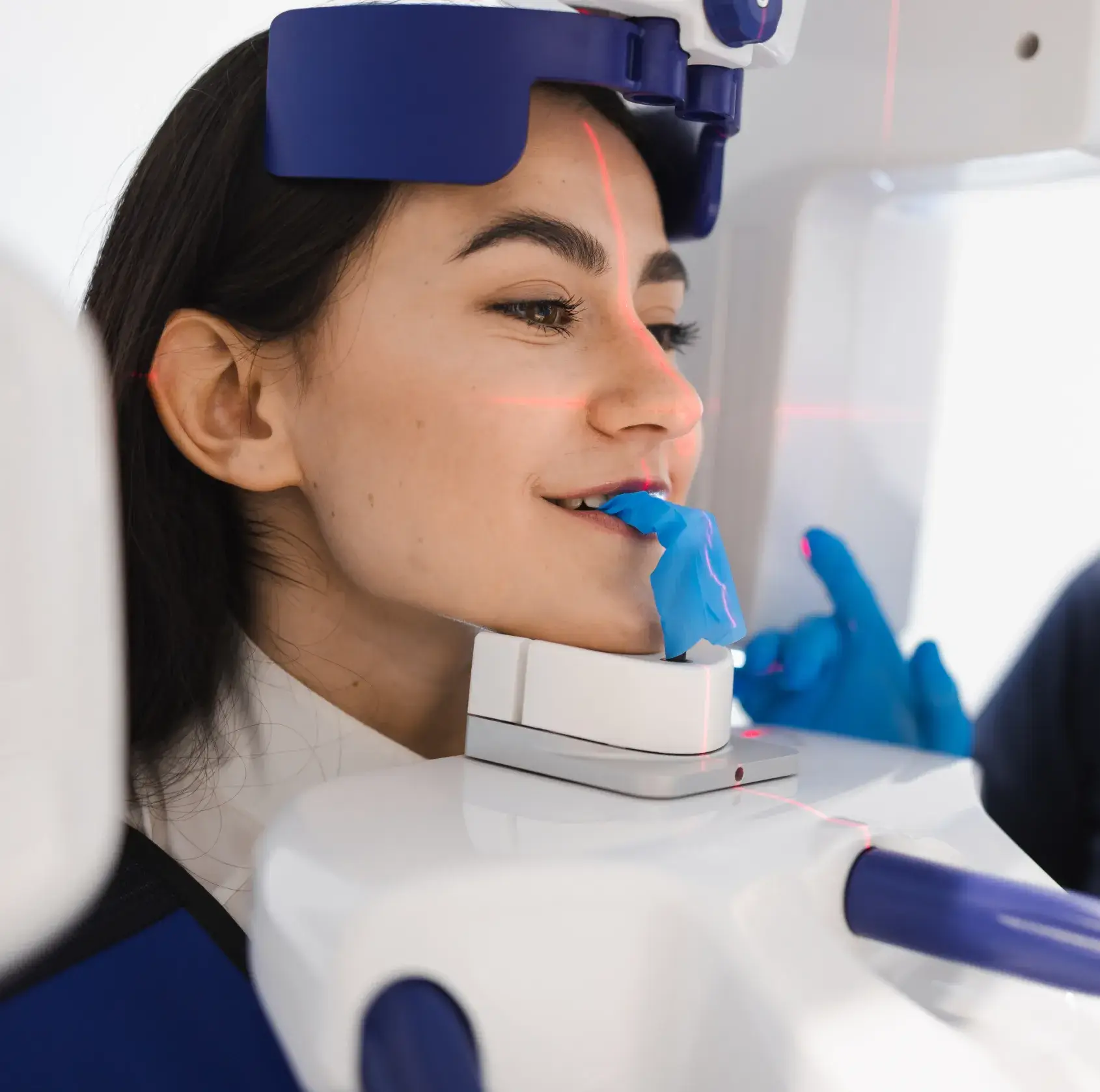 Woman undergoing a dental X-ray scan with a bite block in her mouth and red positioning laser lines on her face.