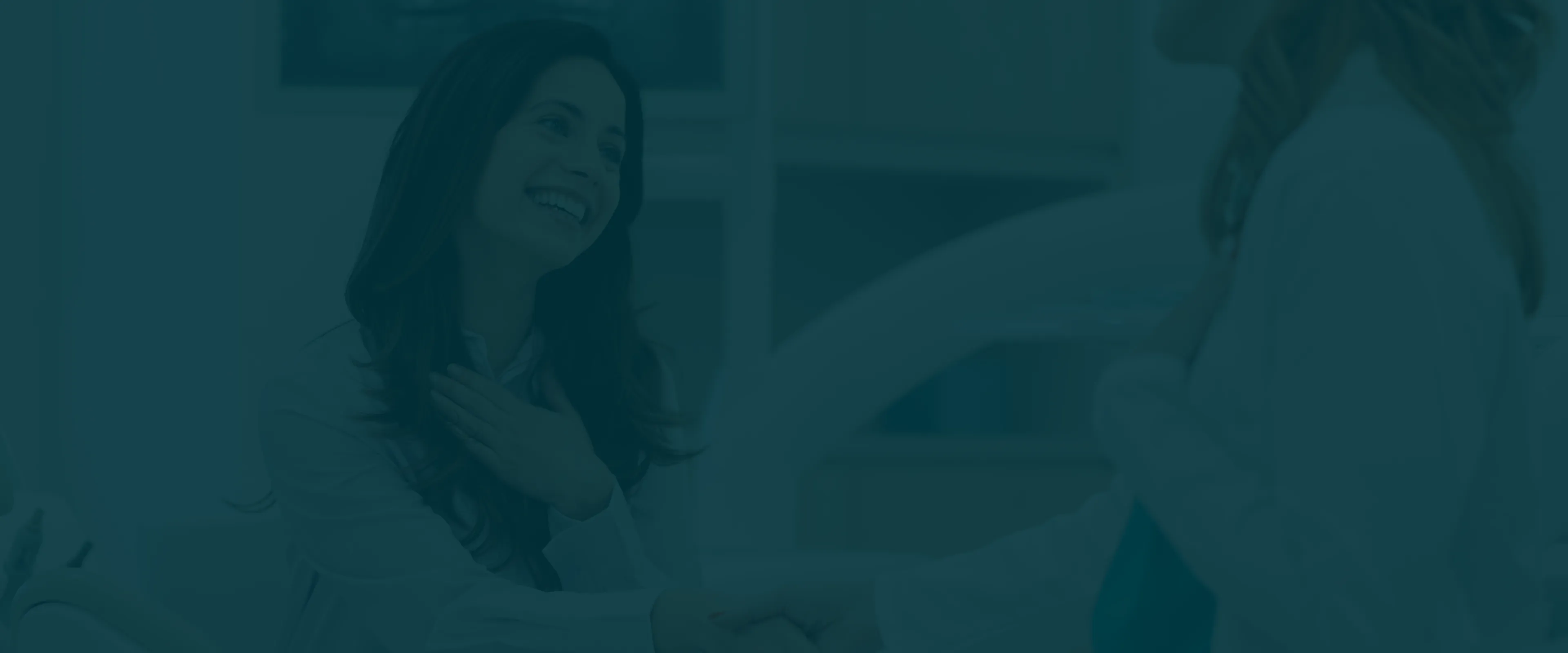 A woman smiles warmly while shaking hands with another person, expressing friendliness and agreement.