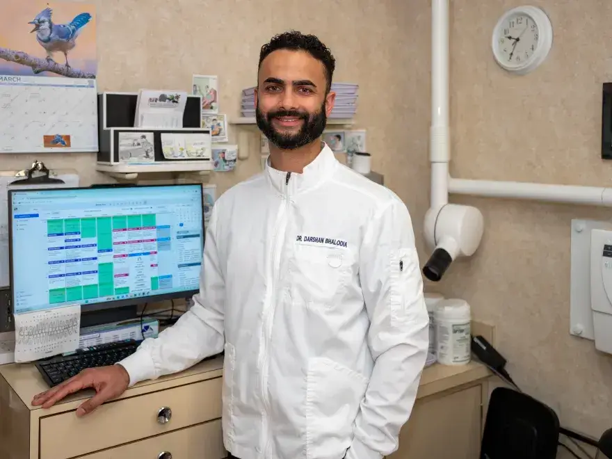 Smiling man in white coat standing next to computer with a scheduled calendar on screen.