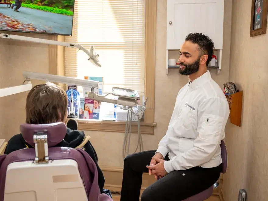 Dentist in white coat sitting and talking with a patient seated in a dental chair.