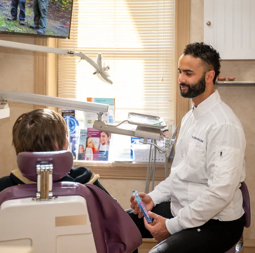 Dentist in white coat explaining toothpaste benefits to patient seated in dental chair.