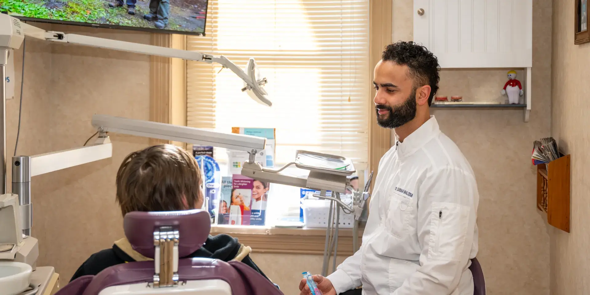 Dentist in white coat talking to patient sitting in purple dental chair with equipment around.