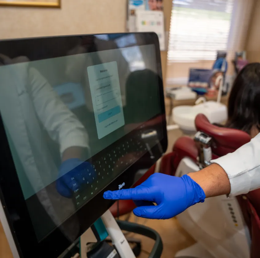 Person wearing blue gloves interacts with touchscreen in a medical or dental office.