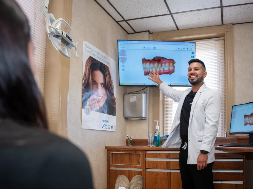 Male dentist in white coat explaining teeth scan on screen to patient in dental office.