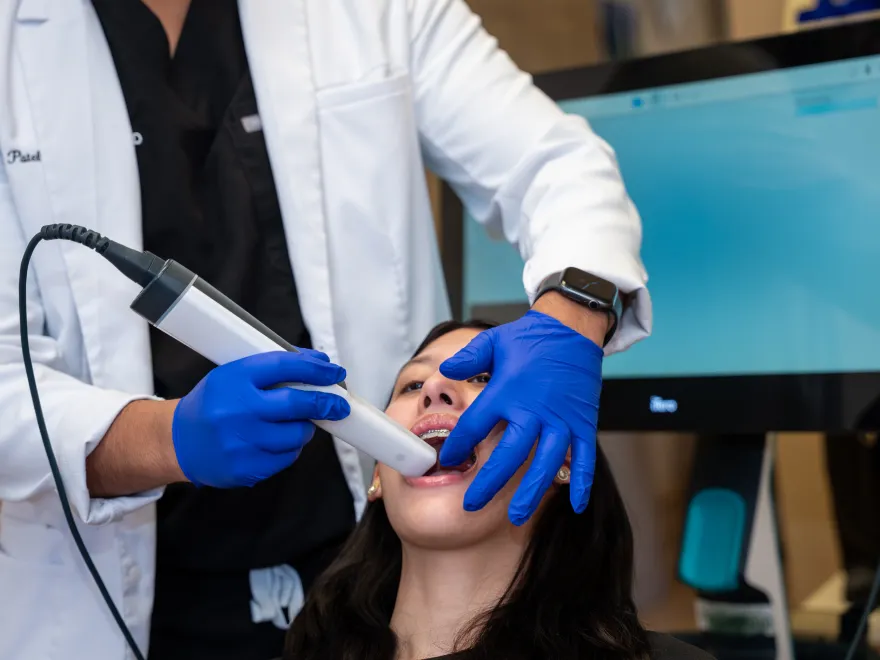 Dentist wearing blue gloves using an intraoral scanner inside a patient's open mouth.