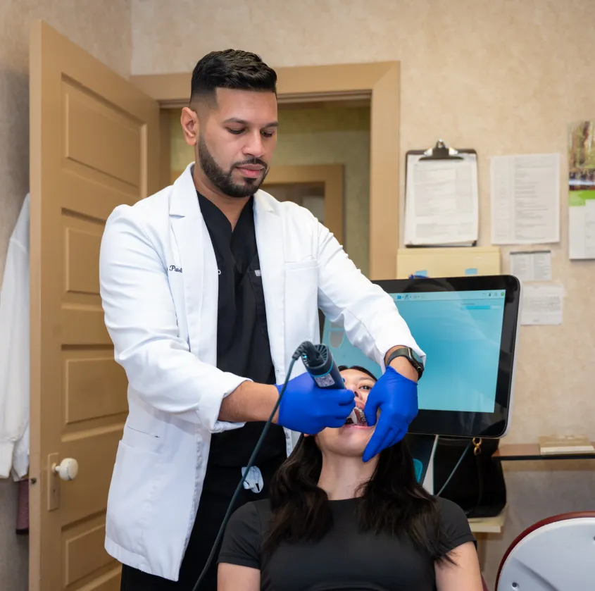 Dentist wearing gloves scans the mouth of a seated female patient in a clinic room.