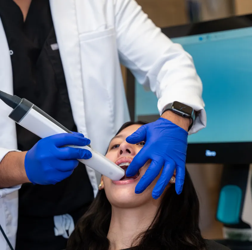 Dentist wearing blue gloves uses dental scanner inside a patient's mouth with braces.