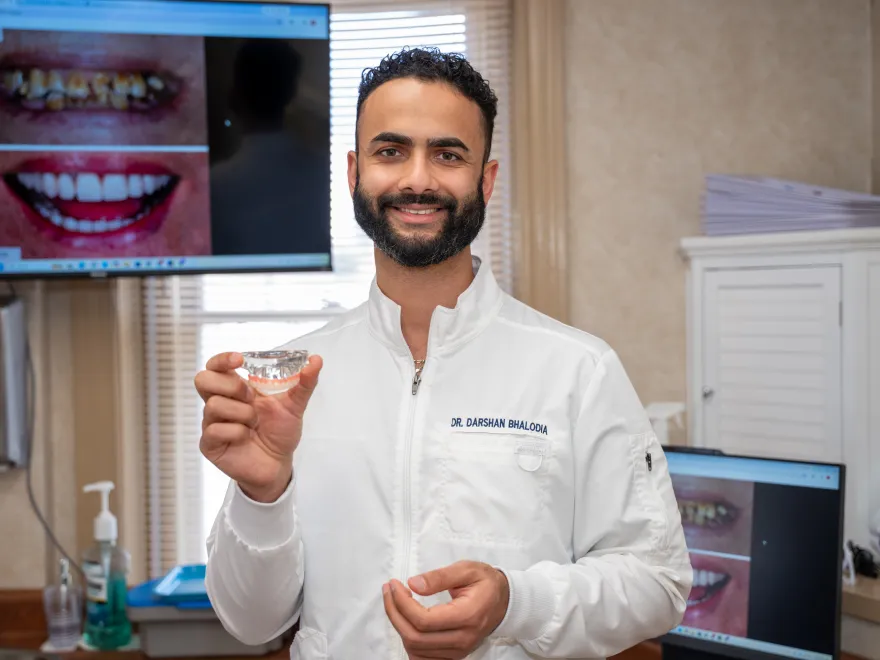 Dentist in white coat holding a dental mold with images of teeth on screens behind him.