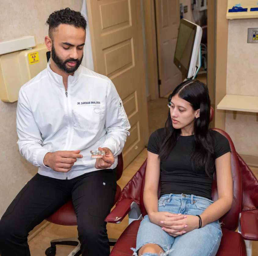 Dentist in white coat explaining teeth model to a seated woman in a dental office.
