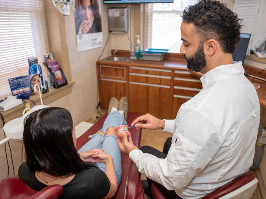 Dentist explaining dental model to patient seated in a dental chair in clinic room.