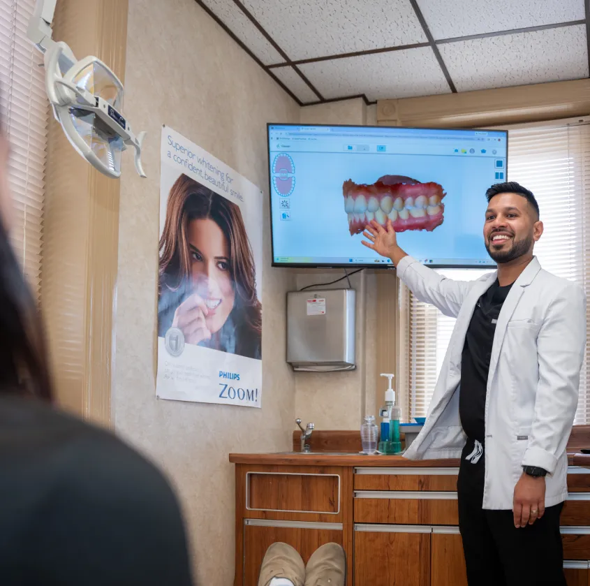 Dentist in white coat showing dental 3D image on screen to patient in exam room.