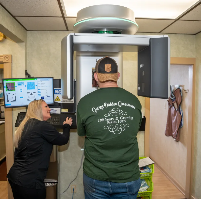 Man in green shirt standing in medical imaging machine while woman in black adjusts controls.