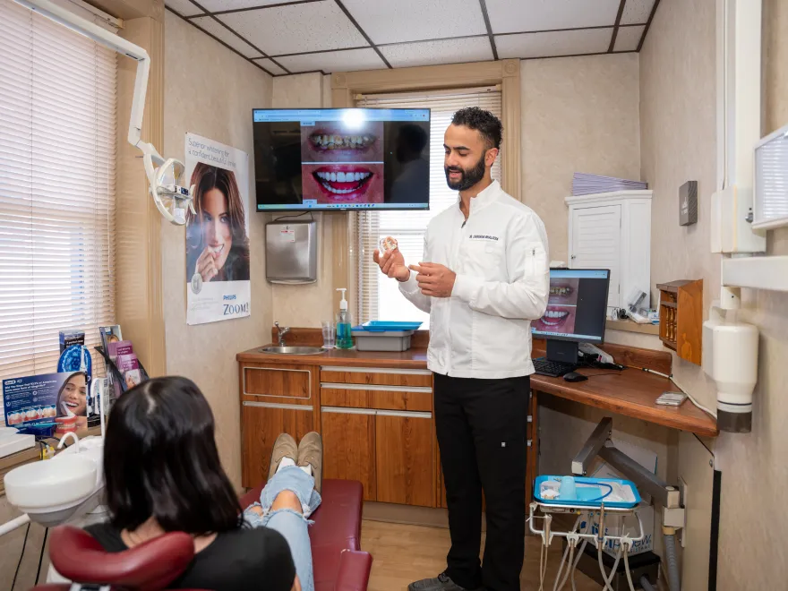 Dentist showing a dental model to a seated patient in a modern dental examination room.