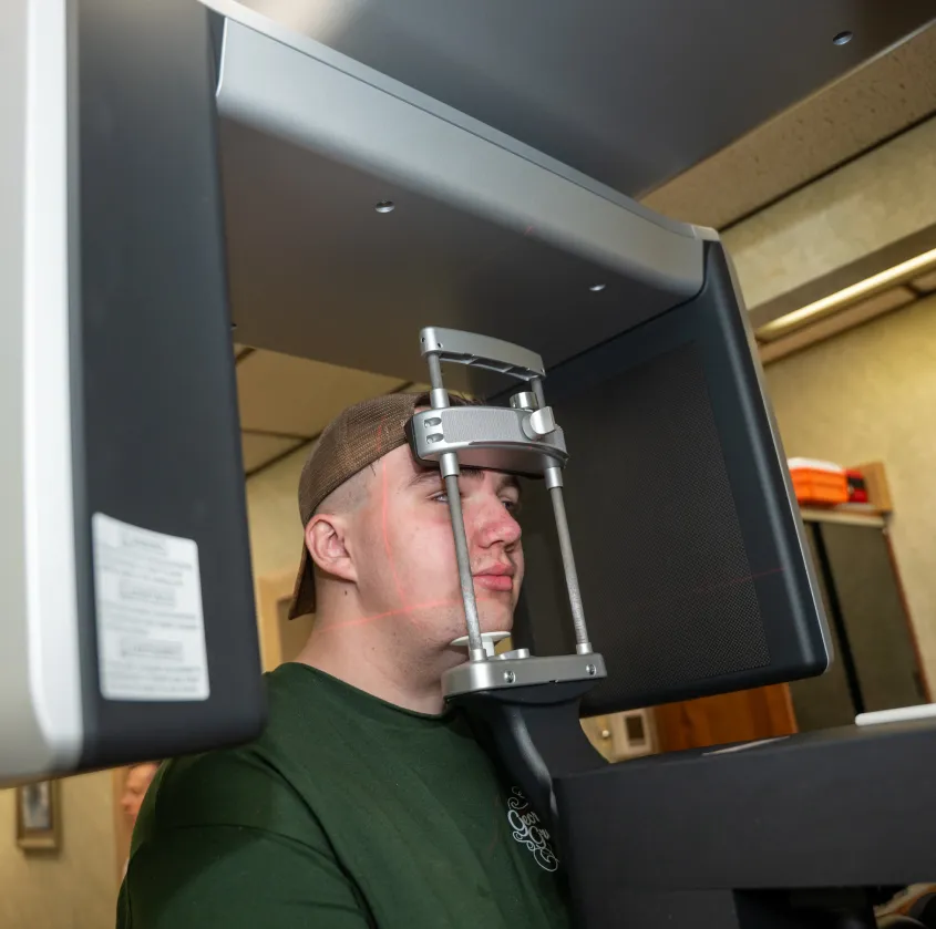 Man wearing a brown cap undergoing an eye scan with a medical imaging device emitting red laser lines.