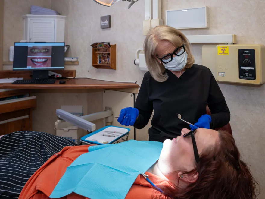 Dentist wearing mask and gloves examining a patient lying back in a dental chair.