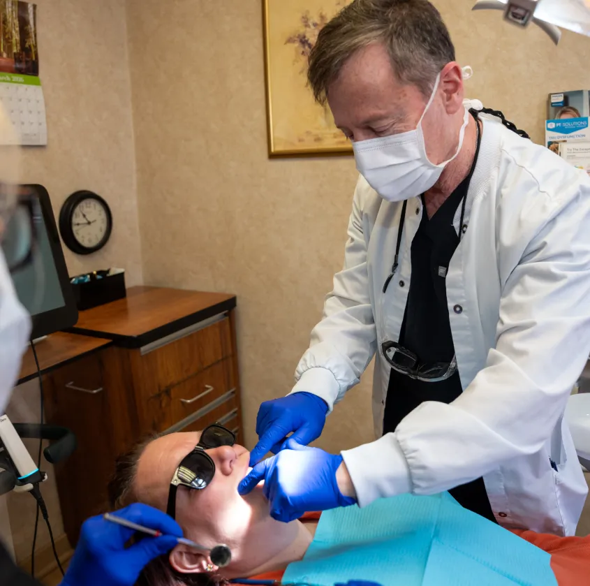 Dentist wearing mask and gloves examining patient's mouth in dental office.