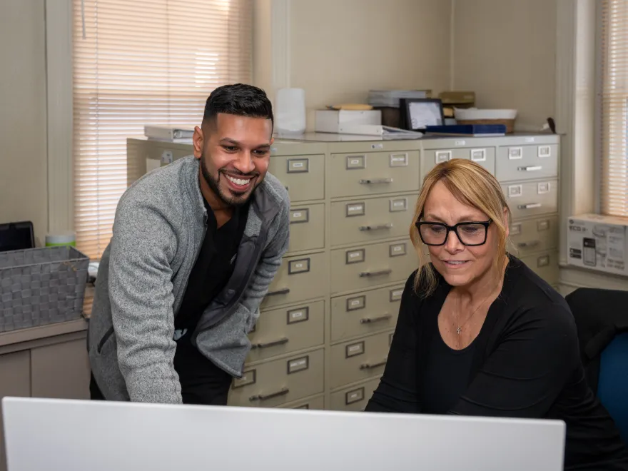 Man and woman working together and smiling while looking at a computer in an office.