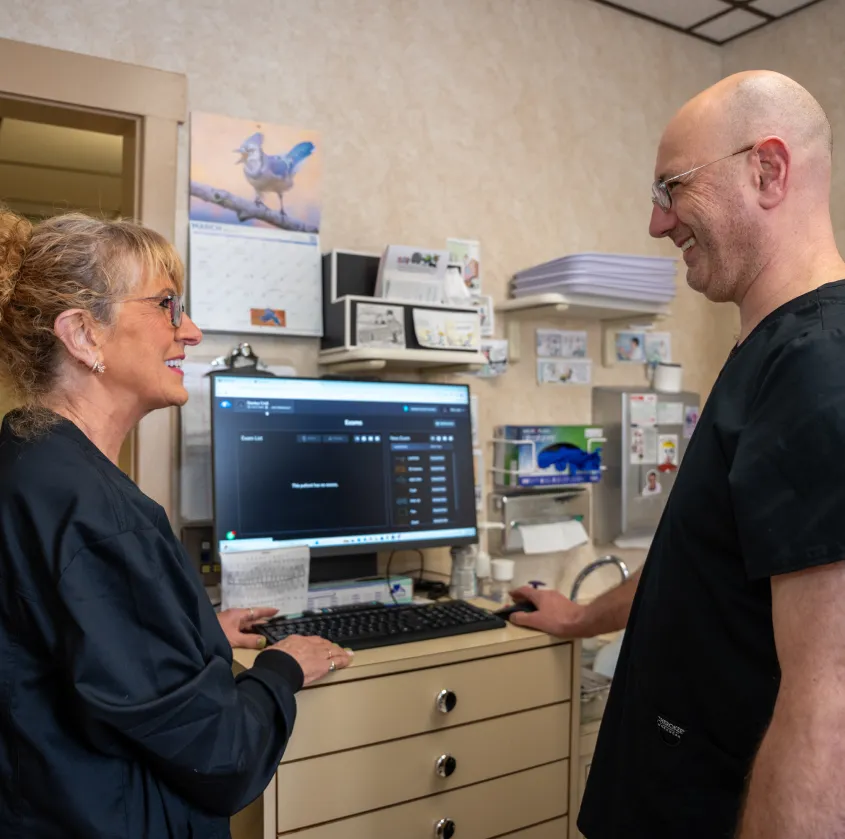 Two medical professionals smiling and looking at a computer screen in a clinic room.