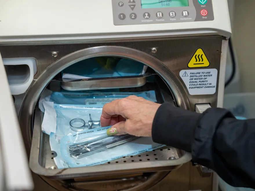 A hand placing dental tools in sterilization pouches inside an autoclave sterilizer machine.