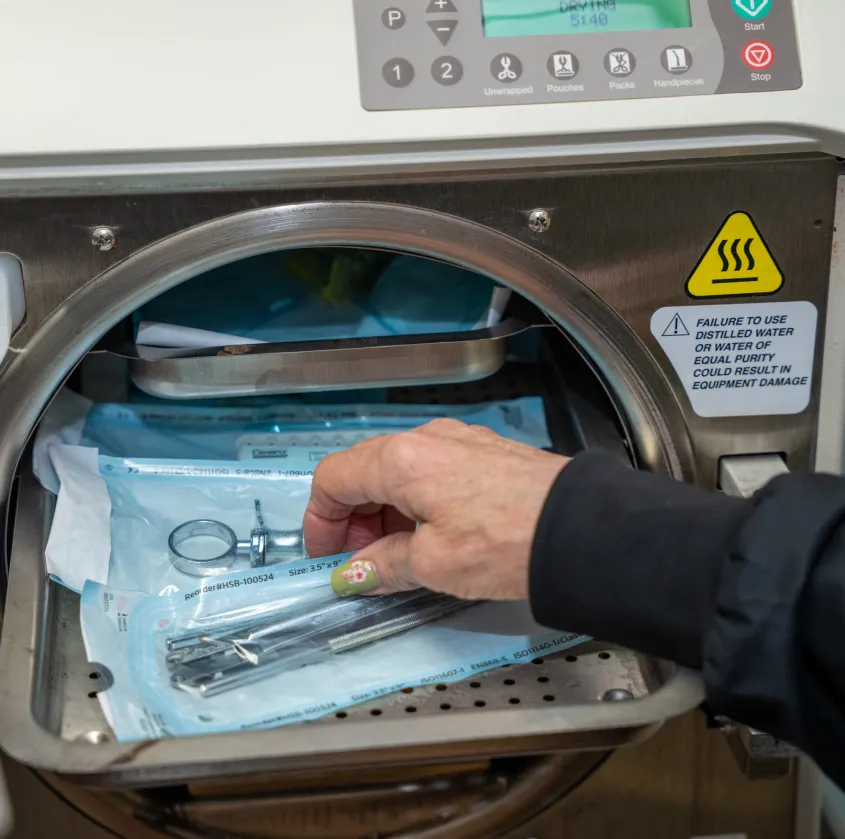 Hand placing dental tools into a sterilizer pouch inside an autoclave machine.
